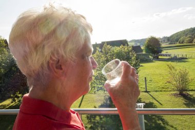 Yaşlı vatandaş bahçede güneşte bir bardak su içiyor
