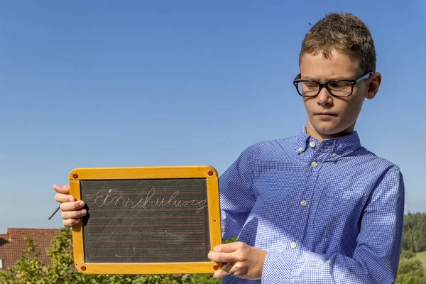 Smart boy with glasses and blackboard on "school enrolment" insists in front of blue sky — Stock Photo, Image