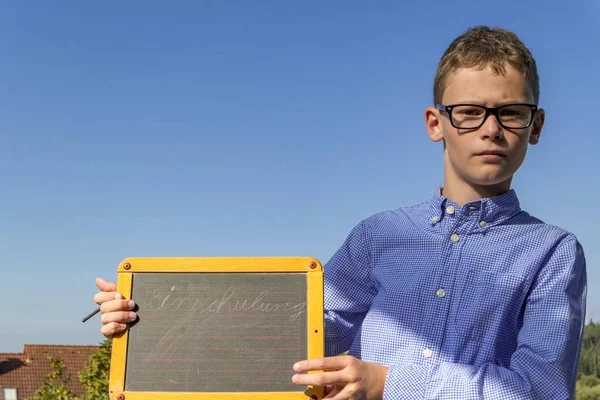 Menino inteligente com óculos e quadro negro em "matrícula da escola" insiste na frente do céu azul — Fotografia de Stock