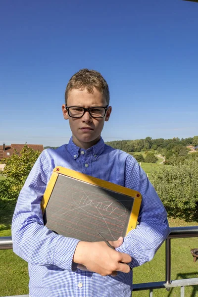 Boy looks angry into the camera and holds a blackboard — Stock Photo, Image