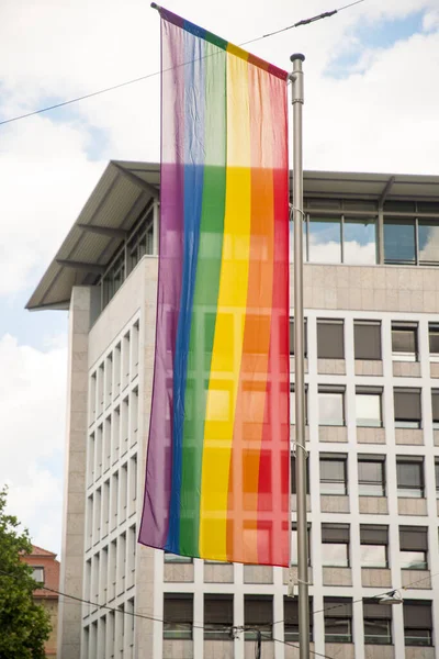 Rainbow flag in front of the windows of a large building