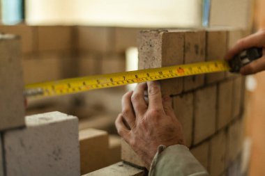 Yuvarlak tuğla duvar inşa ederken iki tuğla arasındaki uzaklığı hesaplamak için bir ölçüm bandı tutan Brickmason