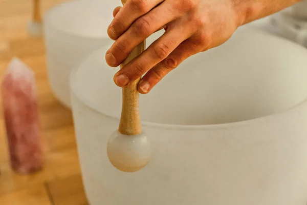Man playing crystal bowls as part of a meditative concert, with Rose Quartz crystal