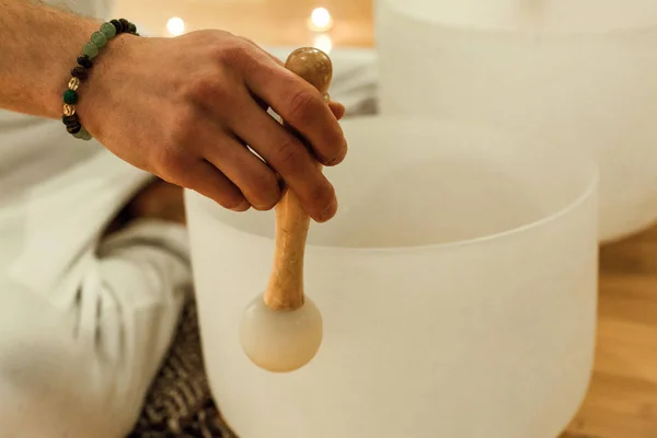 Man playing crystal bowls as part of a meditative concert, with a jade bracelet in his wrist