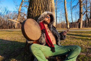 Shaman plays native drum under tree clipart