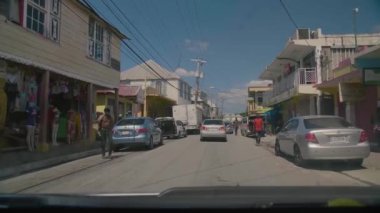 Kalabalık bir köy caddesinde araba hareket ediyor.