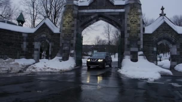 Coche saliendo de la puerta del cementerio durante el invierno — Vídeo de stock