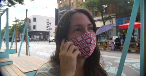 Egy fiatal nő maszkot visel, telefonon beszél. — Stock videók