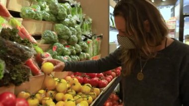 Bakkalda meyveleri kontrol eden kadın maske takıyor.