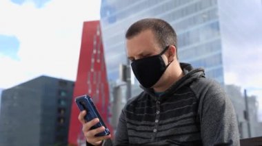 Akıllı telefon kullanan adam bankta maske takıyor.