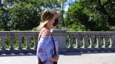 Yüz maskeli ve askı çantalı bir kadın.