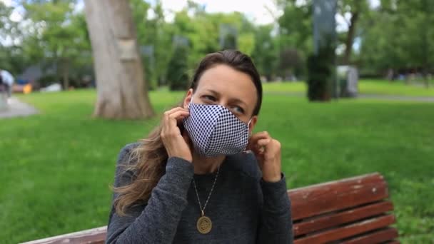 Kvinna sitter på bänk i parken ta bort mask — Stockvideo