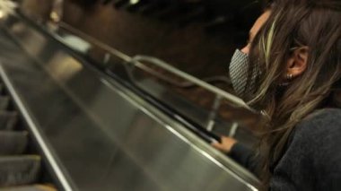 Yürüyen merdivende Covid-19 maskesi takan bir kadın.