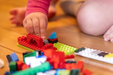 Toddler assembling plastic bricks on a wooden floor, developing fine motor skills and creativity through playtime