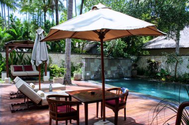 2009.10.11, Ubud, Bali. Şezlong ve şemsiyeler yüzme havuzu ve palmiye ağaçları etrafında yakın. Endonezya'nın deniz manzarası.