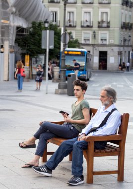 2017.05.31, Madrid, Ispanya. Madrid sokaktaki insanlar. Sokaktaki bankta oturan yaşlı bir adam ve genç bir çocuk. Beni adın olarak ara..