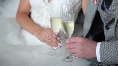 Gelin ve damat şampanya bardakları ellerinde tutuyor. Genç bir çift bir düğünde beyaz köpüklü şarap içer. Gelin ile damat kanepede oturan şampanya içiyor.