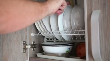 Bir adam mutfak dolap açar ve bir tabak alır.