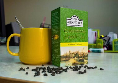 Ahmad Çay - Barut Yeşil Çay fincan ile ofis masasında. Yeşil çay Ahmad bir kutu sarı kupa veya fincan yanında masada ofiste. Masaya dağınık kaynak. 100 gramlık bir paket. Kompozisyon.