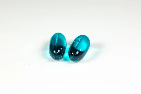 Two clear blue pills against the while surface of a pharmacy table.