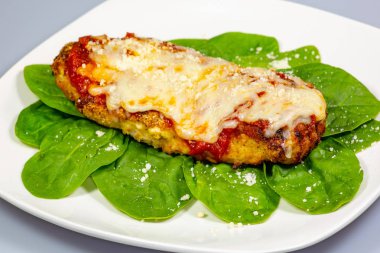 Ispanak yatağında beyaz tabakta üzerine taze parmesan peynir serpin ile tavuk Parmesan