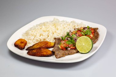 Bir biftek pico de gallo plantain ve beyaz pirinç beyaz tabakta çevrili kaplı. Küba yemekleri