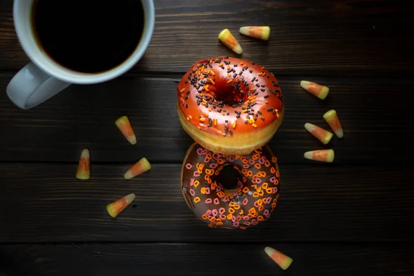 Halloween and Autumn colored tasty colorful donuts served for breakfast on a kitchen table with piping hot coffee.
