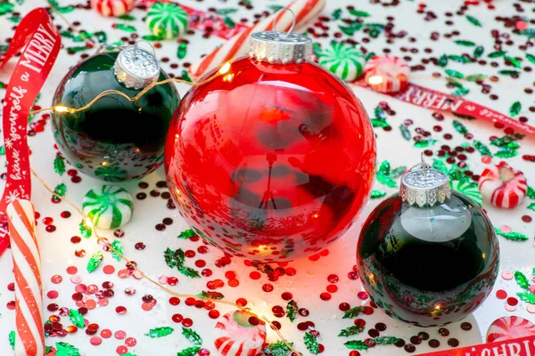 Decoration with red fluid filled Christmas ornament ball and two green filled ornament balls surrounded by a red Have Yourself A Merry Christmas ribbon, a set of Christmas lights and peppermint candy