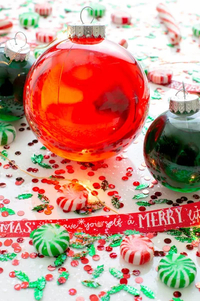 Decoration with red fluid filled Christmas ornament ball and two green filled ornament balls surrounded by a red Have Yourself A Merry Christmas ribbon, a set of Christmas lights and peppermint candy