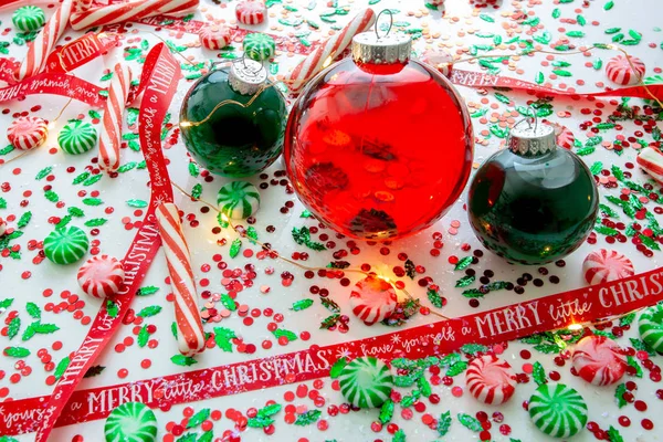 Decoration with red fluid filled Christmas ornament ball and two green filled ornament balls surrounded by a red Have Yourself A Merry Christmas ribbon, a set of Christmas lights and peppermint candy