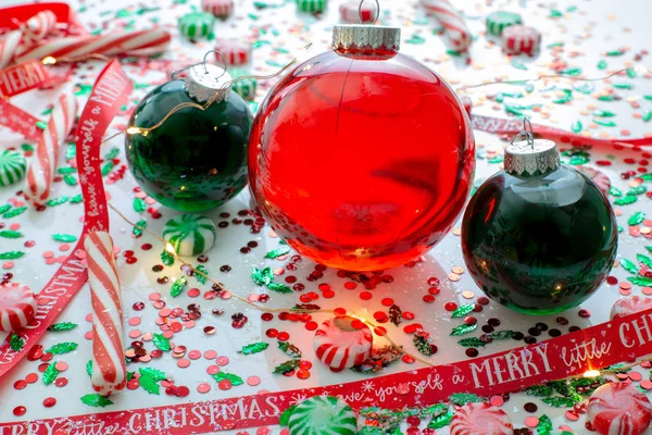 Decoration with red fluid filled Christmas ornament ball and two green filled ornament balls surrounded by a red Have Yourself A Merry Christmas ribbon, a set of Christmas lights and peppermint candy