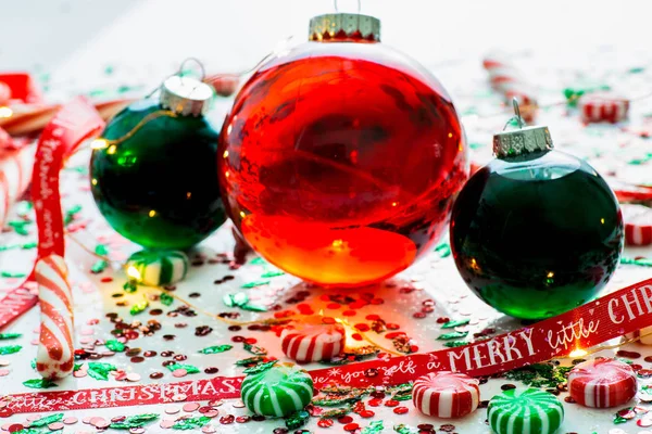 Decoration with red fluid filled Christmas ornament ball and two green filled ornament balls surrounded by a red Have Yourself A Merry Christmas ribbon, a set of Christmas lights and peppermint candy