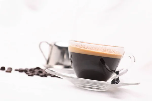 Sıcak siyah kahve kahve çekirdekleri ile beyaz bir arka plan üzerine açık bir cam.