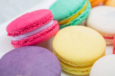 Yakın çekim fotoğraf renkli magaroon bir beyaz seramik tabak içinde yer alıyor. Kahve masasıyla zarif mermer yemek masası.