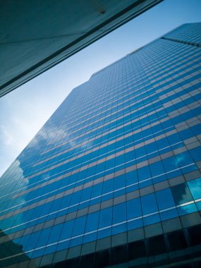 Yüksek binalar ayna yansıması. Beyaz bulutlar ve yüksek binalar bardak mavi gökyüzü gölge yansıtır.