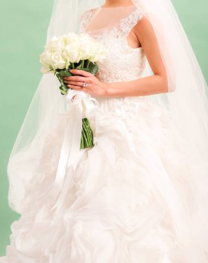 Gelin düğün buketi, gelinlik, düğün detayları, açık yeşil arka planı üzerinde tutar.