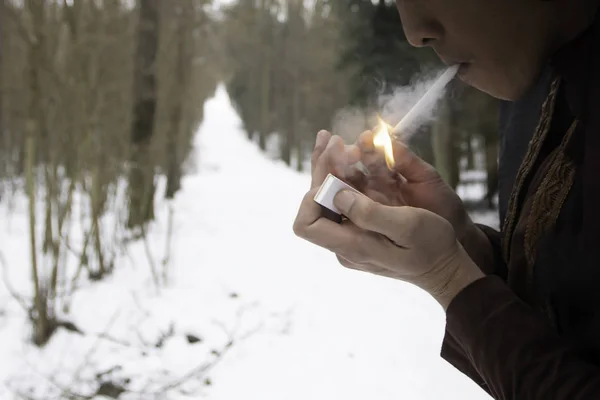 特写人抽着打火机与火柴与粗糙的手在白雪覆盖的松树林 — 图库照片