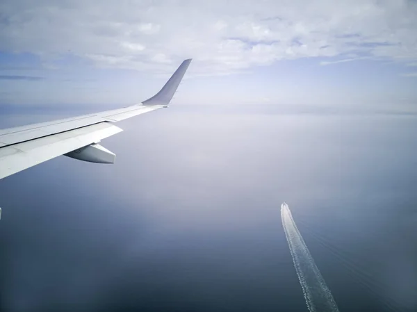 wings of  plane during the flight look from the passenger window. There are not many white clouds in the blue sky above the ground, overlooking the sea of Japan and the boat below.