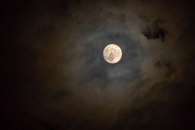 Bulutlu bir günde gökyüzünde parlayan karanlık gecede dolunay.