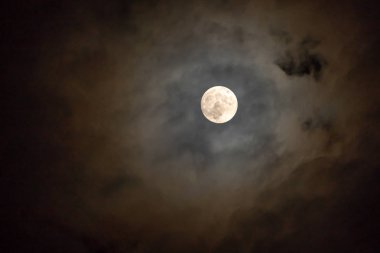 Bulutlu bir günde gökyüzünde parlayan karanlık gecede dolunay.