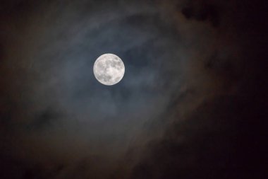Bulutlu bir günde gökyüzünde parlayan karanlık gecede dolunay.