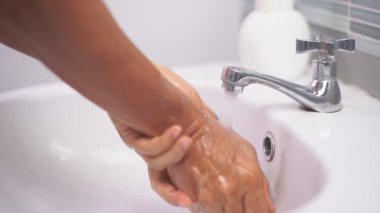 Adamın biri, Coronavirus enfeksiyonunu önlemek için musluk altında elini sabunla ve suyla yıkıyor.