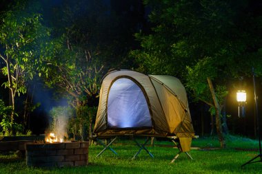 Kamp çadırı ve gaz lambası çimlerin üzerinde, odun sobasının yanında.