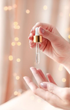 Hafif bir bokeh arka plan üzerinde serum ile güzel bakımlı kadının elleri. Temiz ve yumuşak ciltler için besleyici yağ.