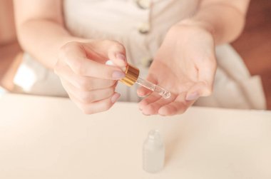 Güzel bakımlı kadının elleri ve hafif bir arka plan üzerinde serum. Kışın temiz ve yumuşak ciltler için besleyici yağ.