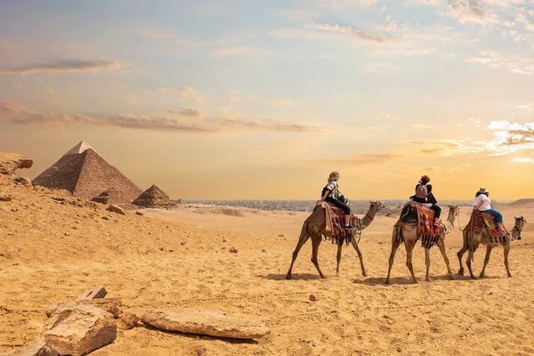 Touristes européens chevauchant des chameaux près des pyramides d'Egypte — Photo