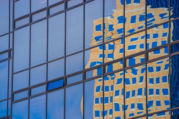 Karşıt gökdelenlerin cam ve metallerinde yansıyan binanın çarpık görüntüsü.