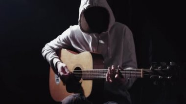 Adsız gizemli Kapşonlu müzisyen siyah arka planı akustik gitar çalmak