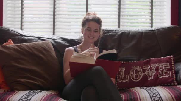 Щаслива Молода Жінка Читає Книгу Відпочиває Дивані Вітальні — стокове відео