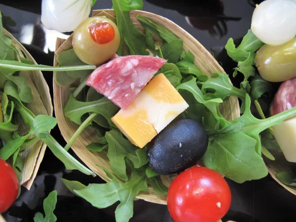 Close up of hors d\'oeuvres on a small oval bamboo bowl on a bed of arugula